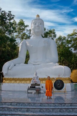 Monk in front of large white Buddha statue